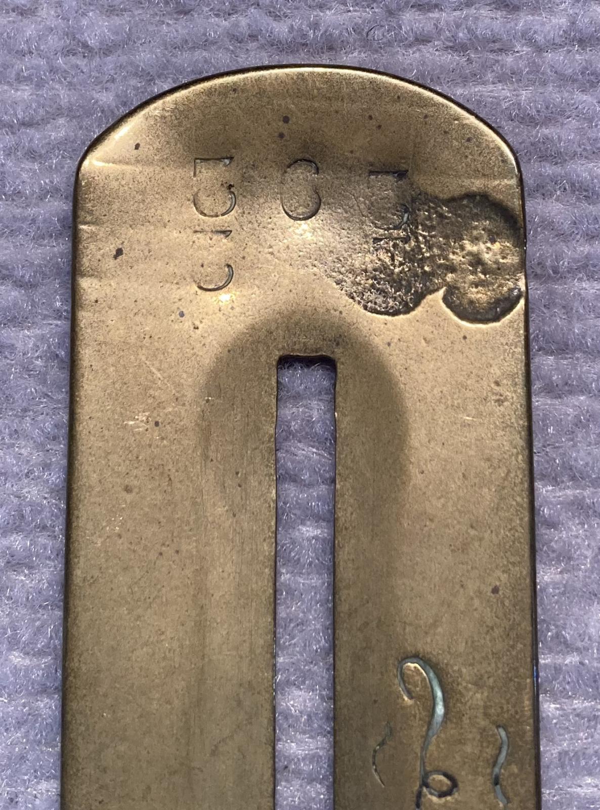 Close up of antique brass button stick showing stamped numbers