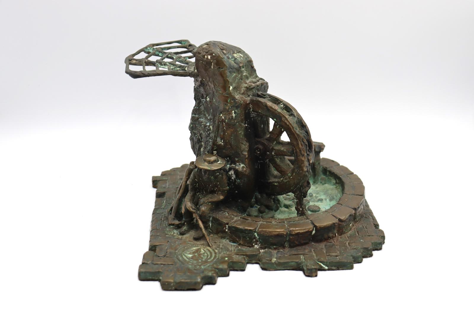 Bronze model of a 'swagman' figure sitting on a circular wall leaning up against a tall pillar of rocks. Emerging from the rock into the pool within the wall is half of a water wheel. On the opposite side of the pillar is a triangular pergola feature.