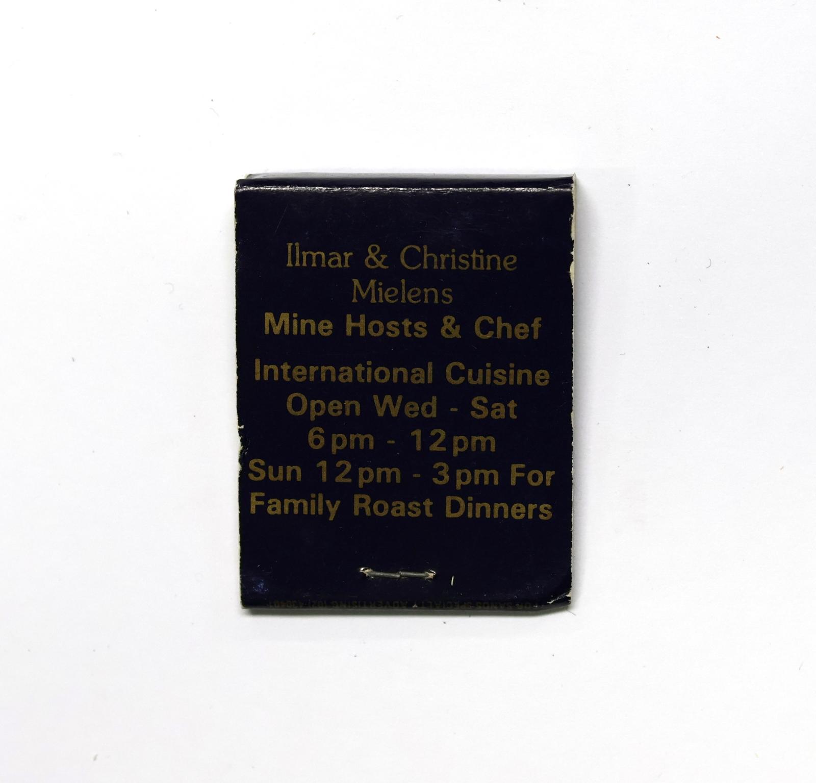 Rectangular shaped matchbook with dark blue background and gold text.  The front of the matchbook has a brown igniting panel. 