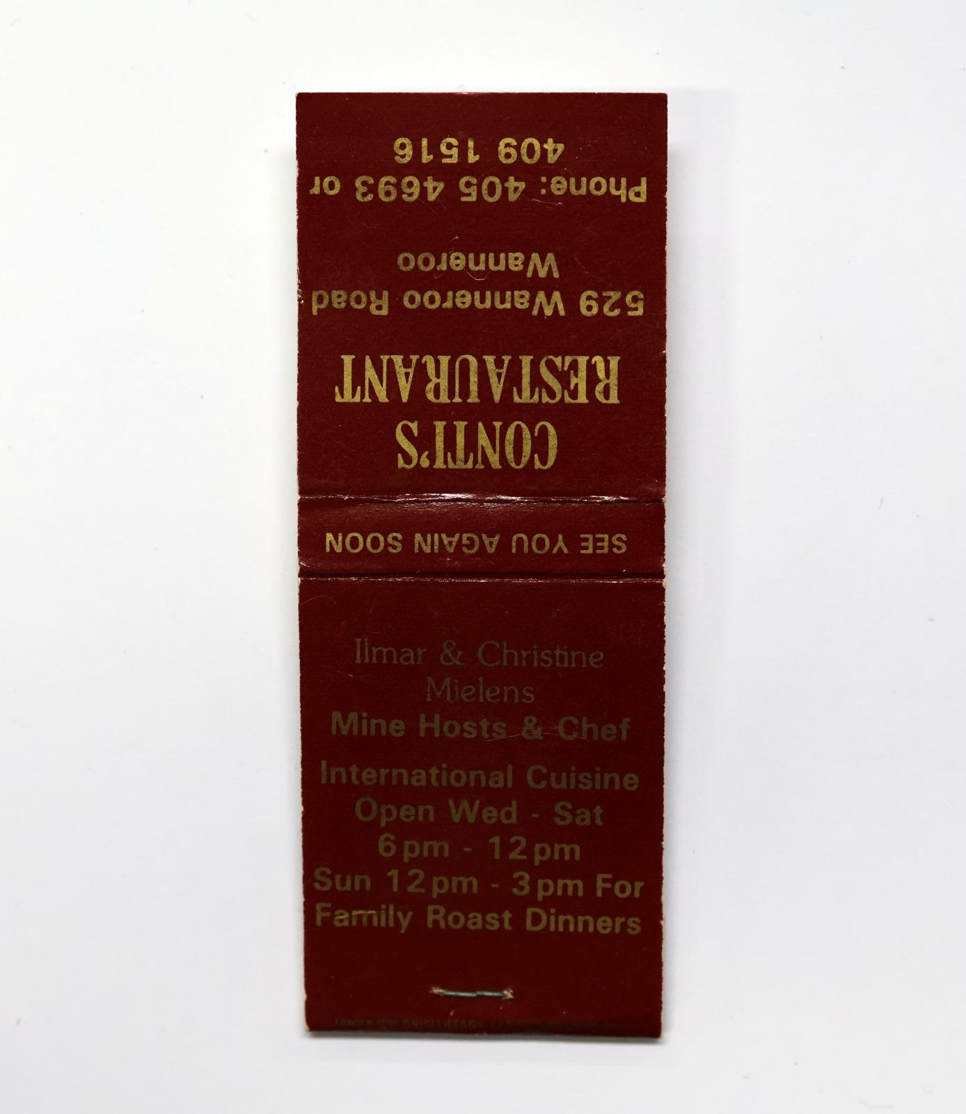 Rectangular shaped matchbook with red background and gold text.  The front of the matchbook has a brown igniting panel. 