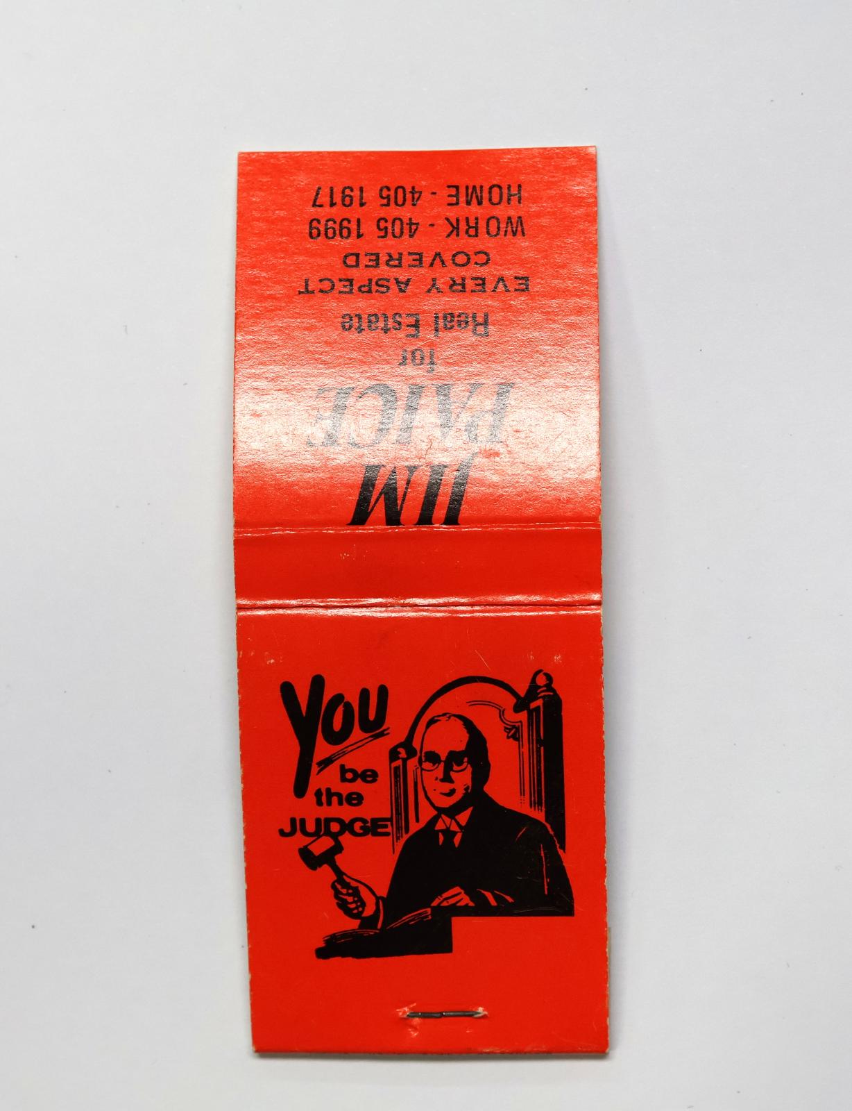 Rectangular shaped matchbook with red background and black text.  The front of the matchbook has a grey igniting panel. The back of the matchbook has an image of a judge with a gavel. 