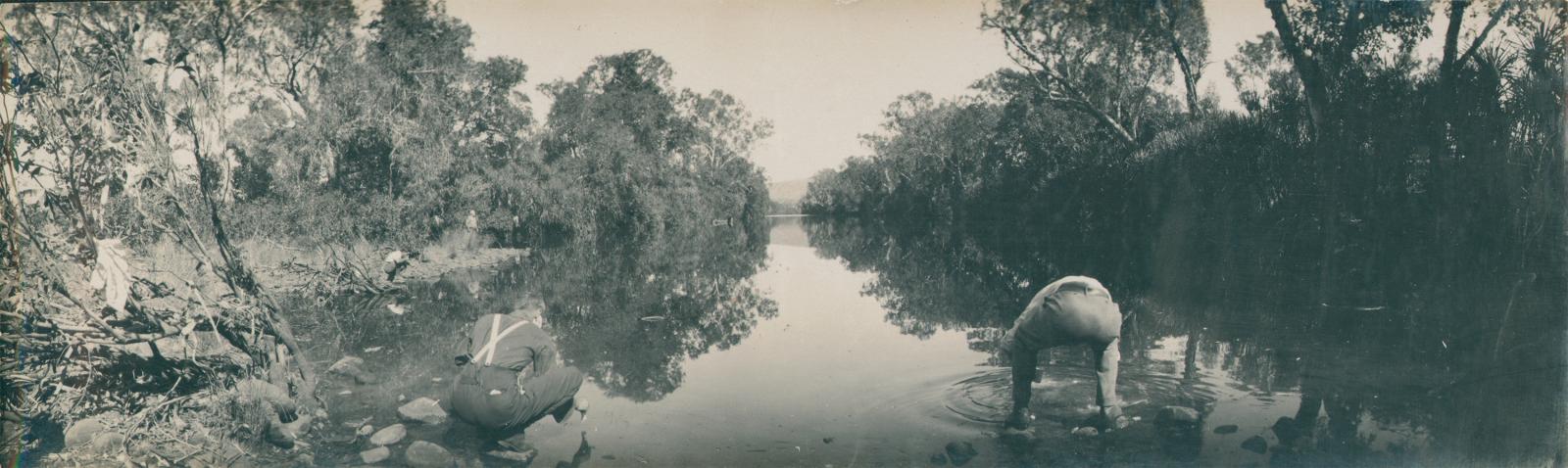 Two men squatting on stones in a river