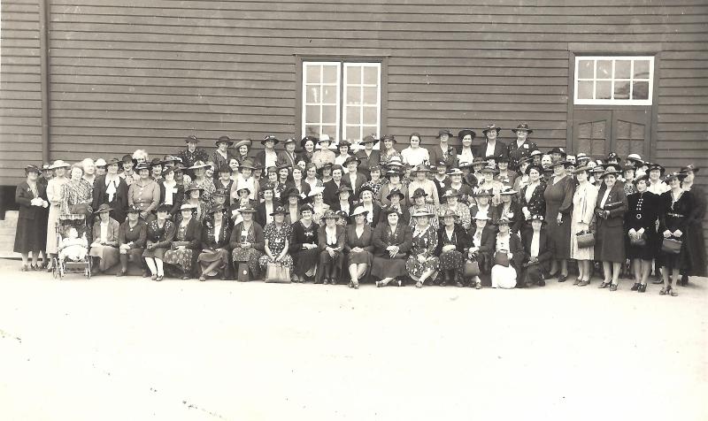 black and white photograph of 50+ women sitting and standing in front of a large building