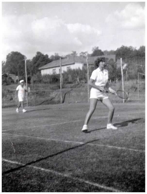 Black and white photograph of two people in white playing tennis on a grass outdoor court