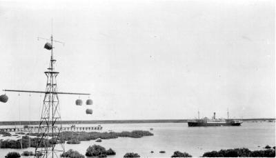 Black and white landscape photograph of Port Hedland harbour showing jetty and ship. 