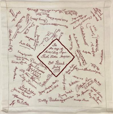 A square white linen voile nurse's veil with embroidered signatures in red thread. 