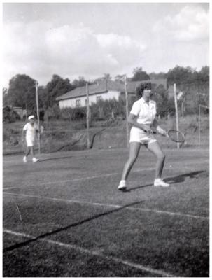 Black and white photograph of two people in white playing tennis on a grass outdoor court