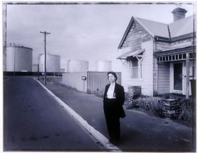 Black and white photograph print of Jemma Dacre standing on the sidewalk in front of an old house