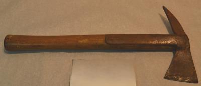 Metal firefighter's axe, with a flat axe head on one side and a pick head on the other. The axe is mounted on a cylindrical wooden handle.