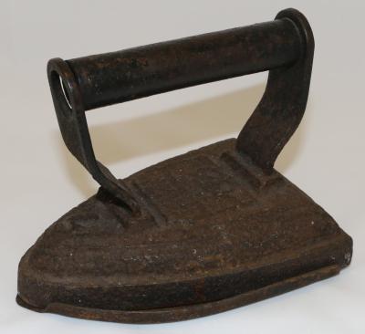 Hand held stove top flat iron with hollow metal cylindrical handle with dent on top attached to cast iron brackets, painted black and welded to iron base. Base heavily corroded. Slightly pointed front with broad flat base.
