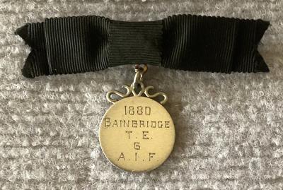 Silver identity badge made from coin suspended on black bow brooch - Trevelyan Ethelbert Bainbridge