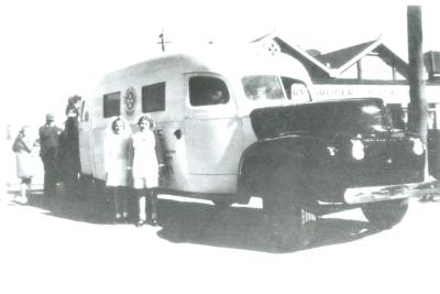 Black and White photograph.  Kellerberrin's 1st ambulance, dedicated by Reverend Pym.  Jennifer Flanders on left, Judith Mather on right