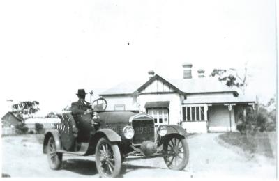 Black and White photograph.  Model T Ford parked outside house in Kellerberrin in unknown street.  Man sitting in vehicle is also unknown