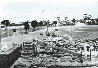 Black and White photograph.  Bagged  wheat stack at flour mill