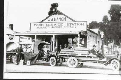 Black and White photograph.  J A Hamon Dealer situated at West Massingham St.  Trucks Tractors Rabbit netting - also 1st fuel bowser in Kellerberrin. Sidney James Forster on truck at front