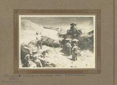 Black and white photograph.  7 men working on Mather's threshing machine and straw press