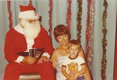 Colour photograph.  1970's.  Marilyn Cox with son, Greg Cox, visiting Santa. Marilyn Cox is married to Norm Cox and is the daughter of Tom and Lil Morgan.