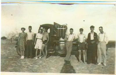 Black and White photograph.  8 people standing in front of old truck