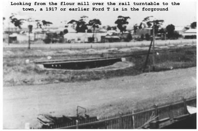 Black and White photograph.  Looking from the Flour Mill over the rail turntable to the town, a 1917 or earlier Ford T is in the foreground