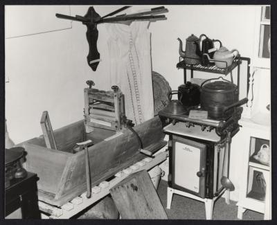 PHOTOGRAPH: MUSEUM DISPLAY,GAS STOVE, WASH TROUGHS AND WRINGER, SAUCEPANS, APRON