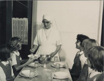 PHOTOGRAPH (COPY): NUN SERVING FOOD TO CHILDREN SITTING AT A TABLE, ST. JOSEPH'S ORPHANAGE