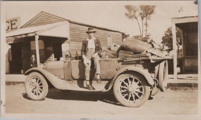 PHOTOGRAPH: AN OLD CAR INFRONT OF WOODEN BARRACKS