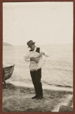 PHOTOGRAPH (DIGITAL): BERT HOLDING A BABY ON THE BEACH, FROM CONGDON FAMILY ALBUM